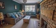 Image shows lounge with large L Shaped Settee, Coffee table, lamps and wood burner