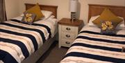 Image shows twin bedroom with bedside table and lamp between the beds
