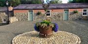 Image shows front of cottages with flower bed in a stone circle