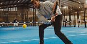 Image shows two individuals playing Padel Tennis on blue court.