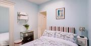 Image shows a double bedroom with side table and lamp and open doorway into ensuite