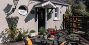 Image is of patio area at back of cottage with wrought iron table and 2 chairs.