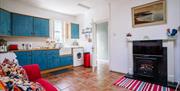 Image shows kitchen and lounge area with all mod cons, sofa, tiled floor, fireplace and rug