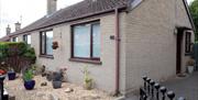 An Image of the front of the semi-detached bungalow with driveway to the side and set of gates.
