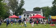 Image shows lots of people enjoy themselves outside of The Ballance House, there is a bouncy castle, lawn games and gazebo's.