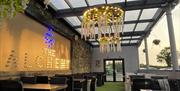An image of a dining area with a feature wall showing the words of The Alchemy in lights and cascading chandeliers hanging from the covered seating ar