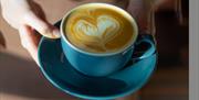 An image of a staff member from Cairo's holding a mug and saucer with coffee inside and a love heart froth.