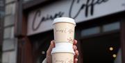 An image of a person holding two take away drinks cups outside Cairo's Coffee