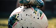 An image of a football with someone holding it in place by their football boot