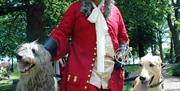 Image is of a man dressed in history costume flanked by two large dogs