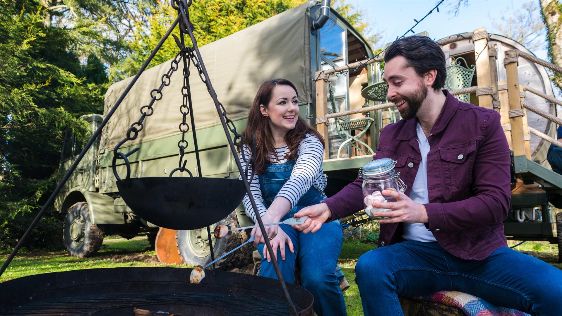 Couple toasting marshmallows over a firepit outside a glamping truck at Larchfield State