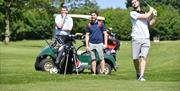 Image is of 3 men on golf course with buggy behind them