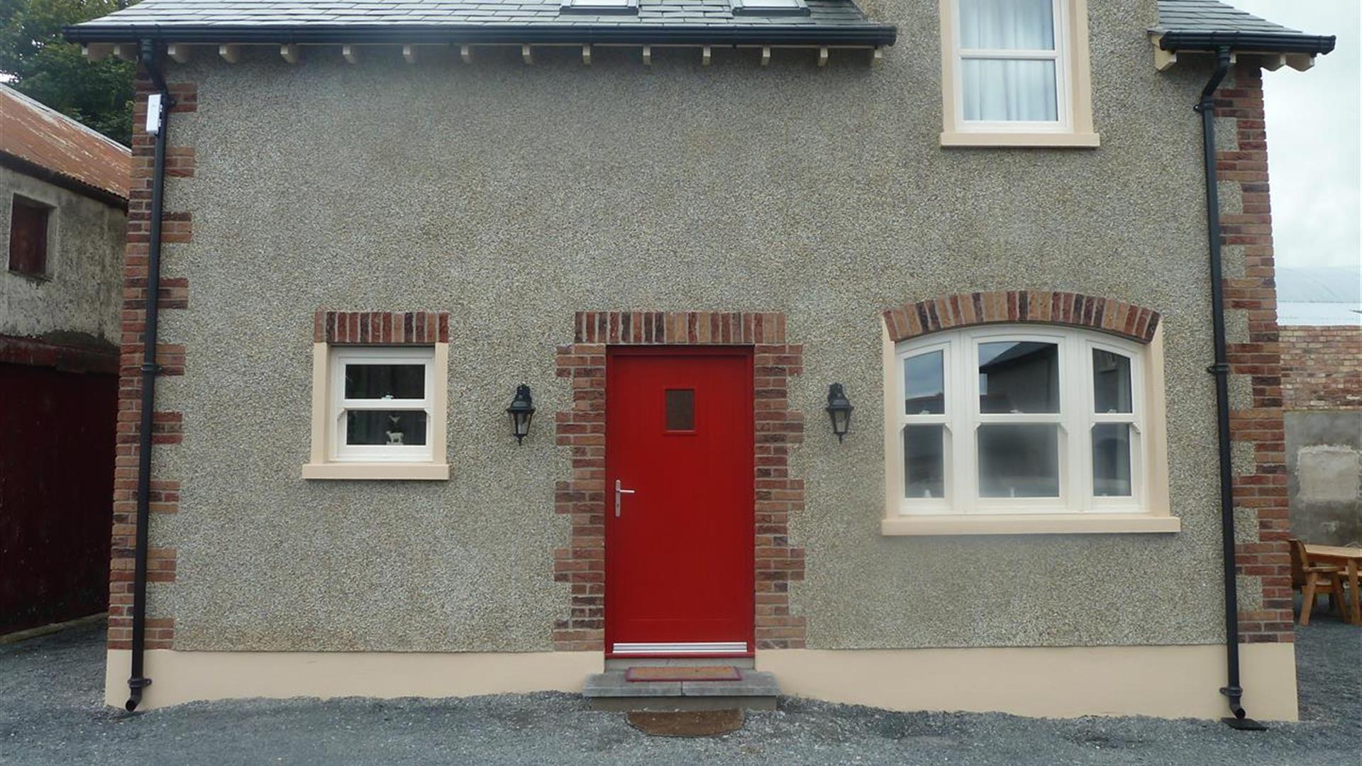 Image shows red front door of stone property with gravel drive