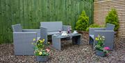Image shows back garden area with rattan seating and low table. Gravel on ground and fence painted green