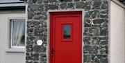 Image is of red front door with stonewall around it and small window to the left of door
