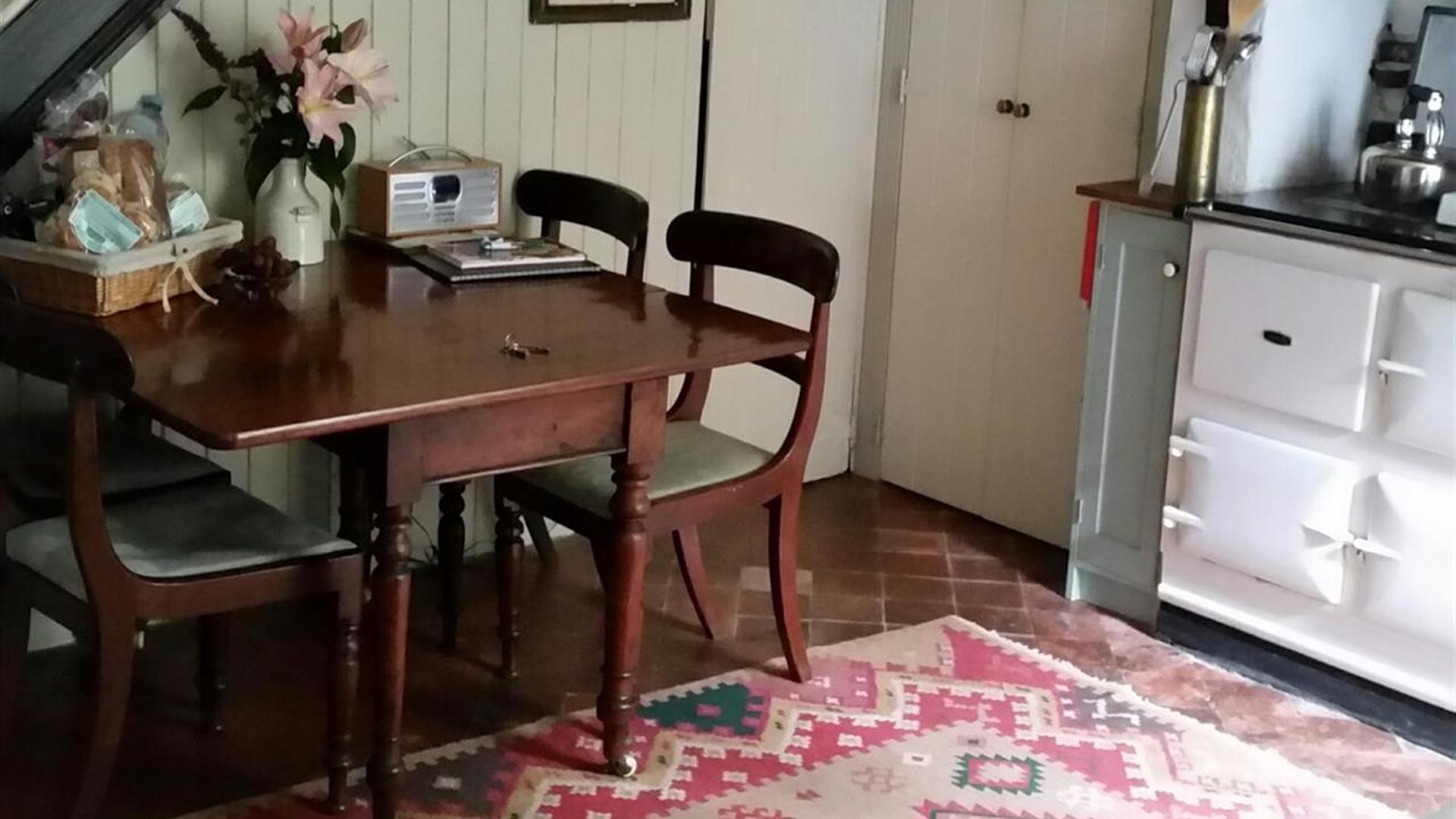 Image shows kitchen dining area with table and four chairs plus Aga