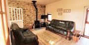 Image shows lounge with leather sofa and armchair, wood burner and TV.