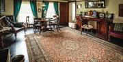 Image is of lounge area with large traditional style rug, armchairs, dining table and chairs and two large windows