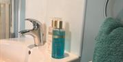 Image shows sink in bathroom with toiletries, towel on towel rail