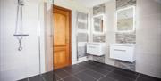 Image shows large shower room with 2 sinks and tiled floor