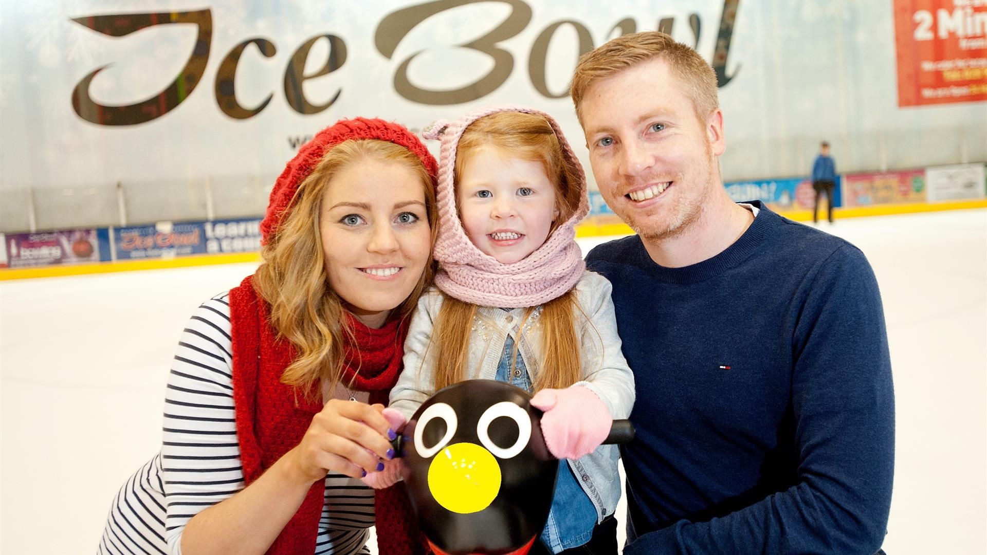Image is of a couple and small child on the ice rink