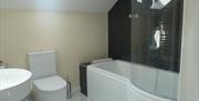 Image shows bathroom with bath and overhead shower, sink and toilet.