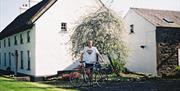Image shows man standing in a garden with a bicycle outside property