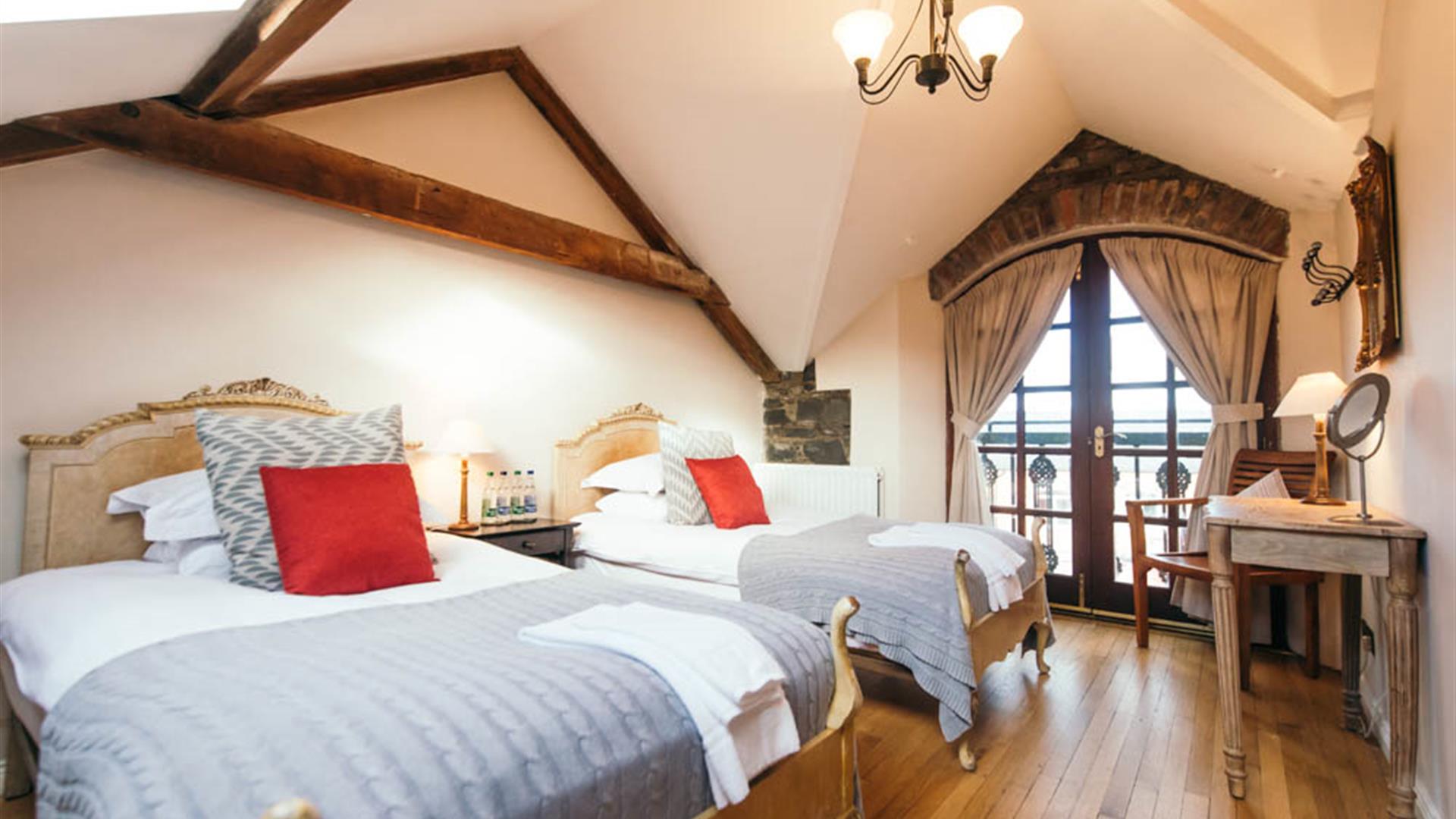 image shows bedroom with double bed and single bed, wooden flooring, exposed beams and dressing table with mirror