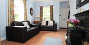 Image shows lounge with 2 leather sofas, tiled floor, wood burner in fireplace with rug in front