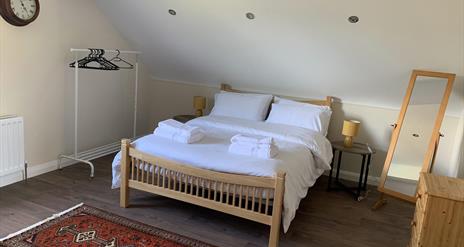 Image shows bedroom in loft with double bed, dressing mirror and clothes rail