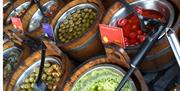 Image shows wooden tubs full of various food stuffs such as olives and cherries