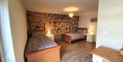 Image shows double bed and single bed in room, tiled floor and feature stone wall.