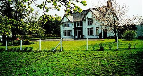 Image shows the front of the property with lawn, fence and trees