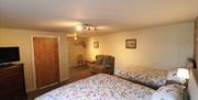 Image shows double bed and single bed in room, tiled floor. Sofa and dresser unit with television sitting on top.