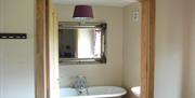 Image shows free standing bath and mirror above through open doorway
