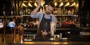 Image shows a bartender making a cocktail behind the bar