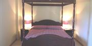 Image shows four poster double bed with side tables and lamps