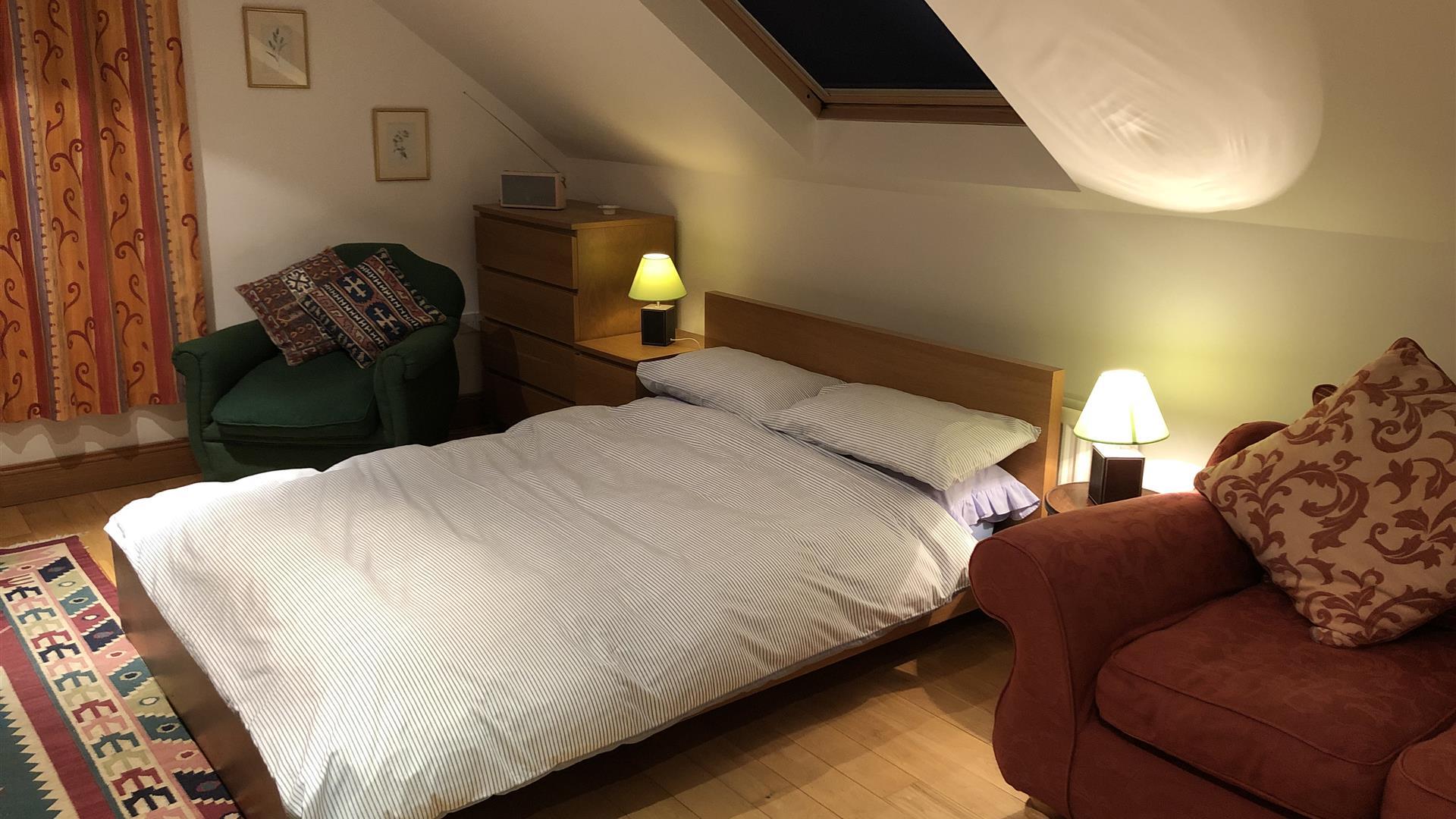 Image shows bedroom with double bed, 2 side tables and 2 chairs. Skylight above the bed.
