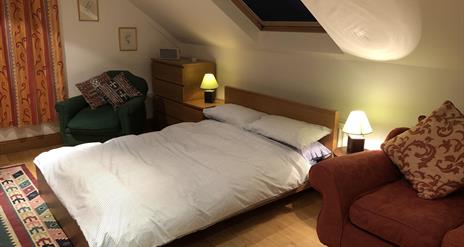 Image shows bedroom with double bed, 2 side tables and 2 chairs. Skylight above the bed.
