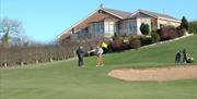 Image shows golfers on course with clubhouse in background