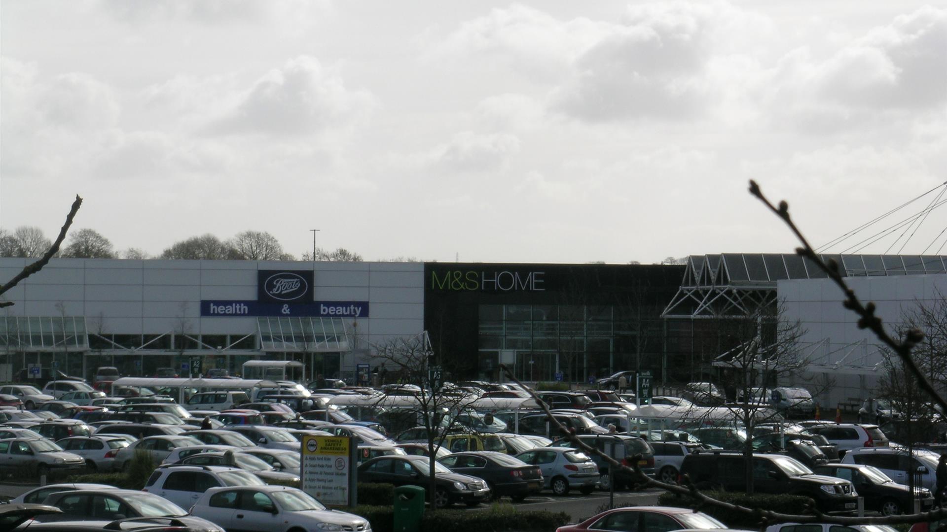 Image is of shop units and car park full of cars