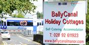 Image shows signage for Ballycanal Holiday Cottages with train arriving in the background