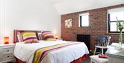 Image shows double bedroom, brick feature wall, black painted radiator, dressing table and chair, beside tables with lamps