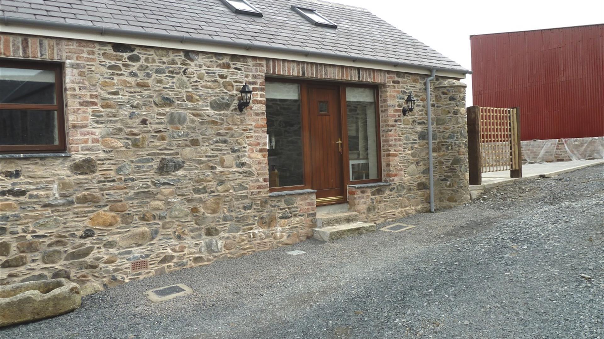 Image shows stone cottage with wooden front door and gravel drive way