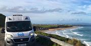 Image is of campervan parked with a view of the beach and the sea