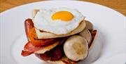 Image shows egg, bacon, sausage, tomato, mushrooms, potato bread on slice of soda bread