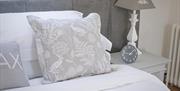 Images shows cushions on bed and clock and lamp on bedside table