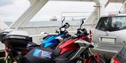 Image shows pair of motorcycles parked on ferry crossing the sea