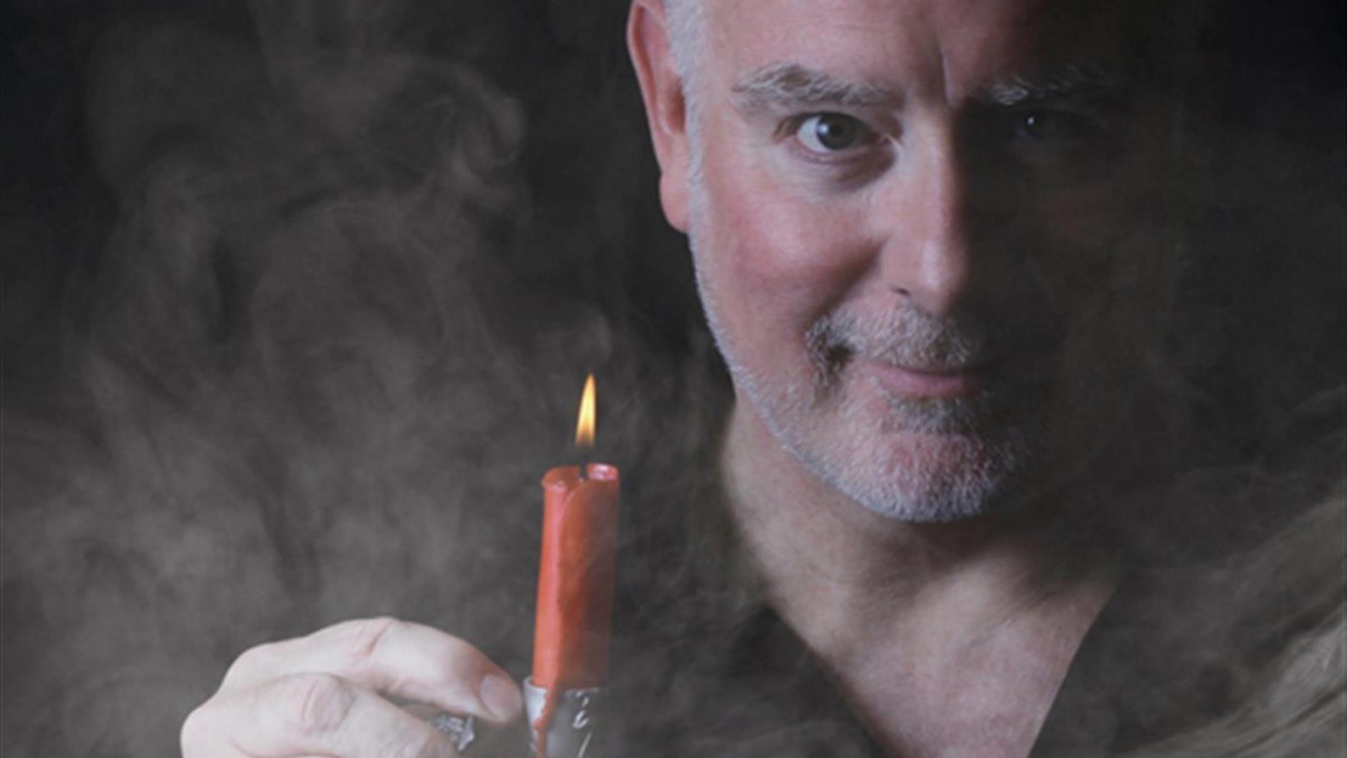 A male actor holding a lit red candle in a candle holder