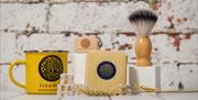 Image is of yellow mug, bar of soap and shaving brush on a wooden table